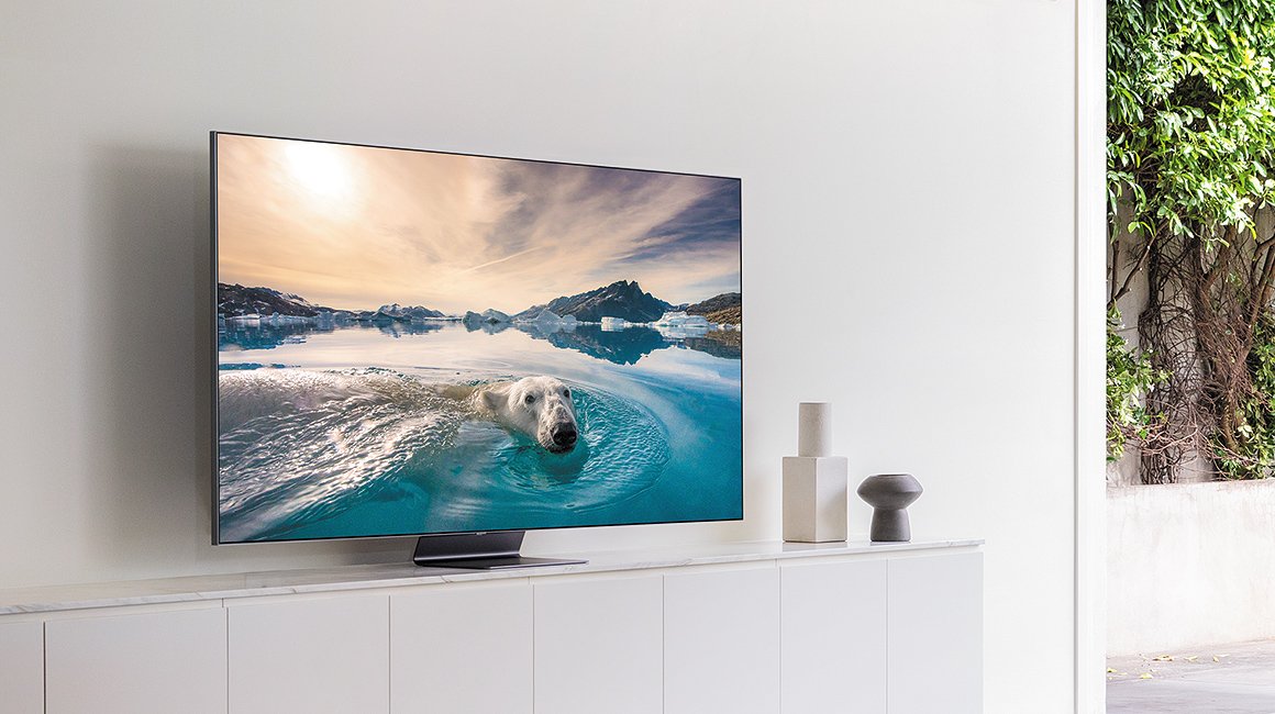 Samsung Smart TVs 2024 and 2025 mounted on a white wall cabinet, displaying a high-resolution image of a polar bear swimming in icy waters under a scenic sky.